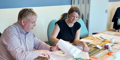 Two people reviewing documents and charts at a meeting table.