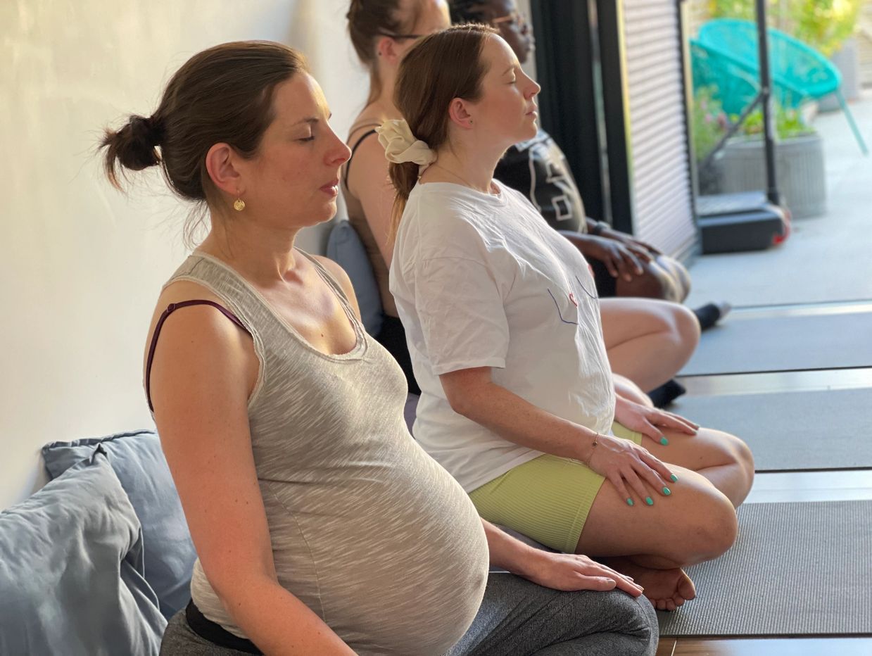 Pregnant women meditating together in a peaceful indoor space.