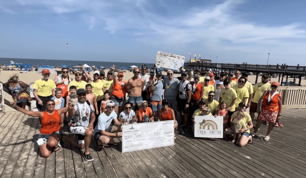 crowd of people gathered at the beach presenting a giant charitable check