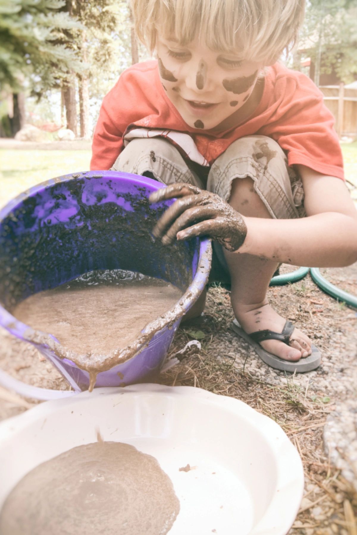 Young boy pouring mud from a bucket to a pie tin