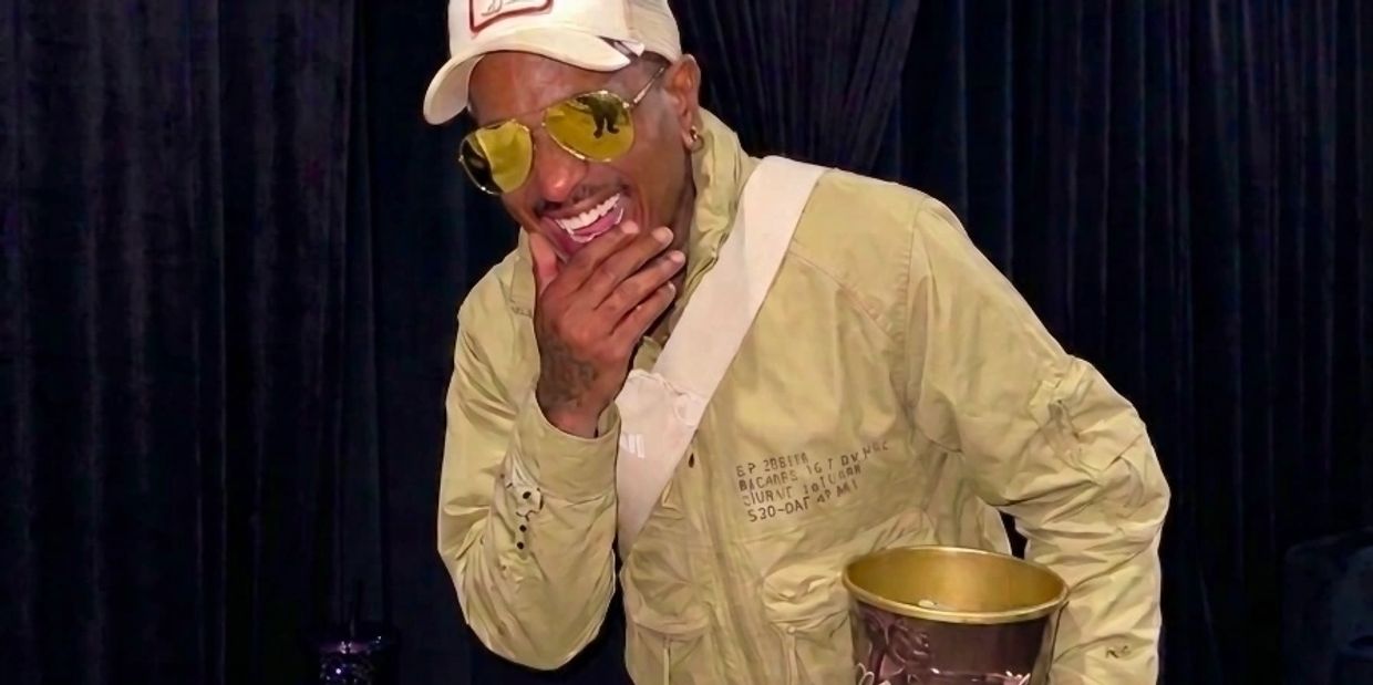 Man in yellow jacket and hat laughing, holding a golden cup.