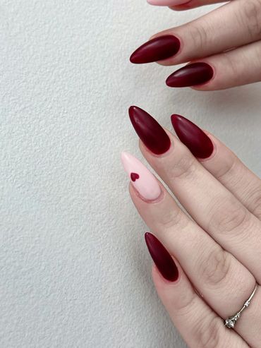 Matte burgundy nails with a single pink accent nail featuring a small heart design.