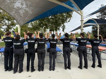 Group of explorers raising hands under shaded outdoor pavilion.