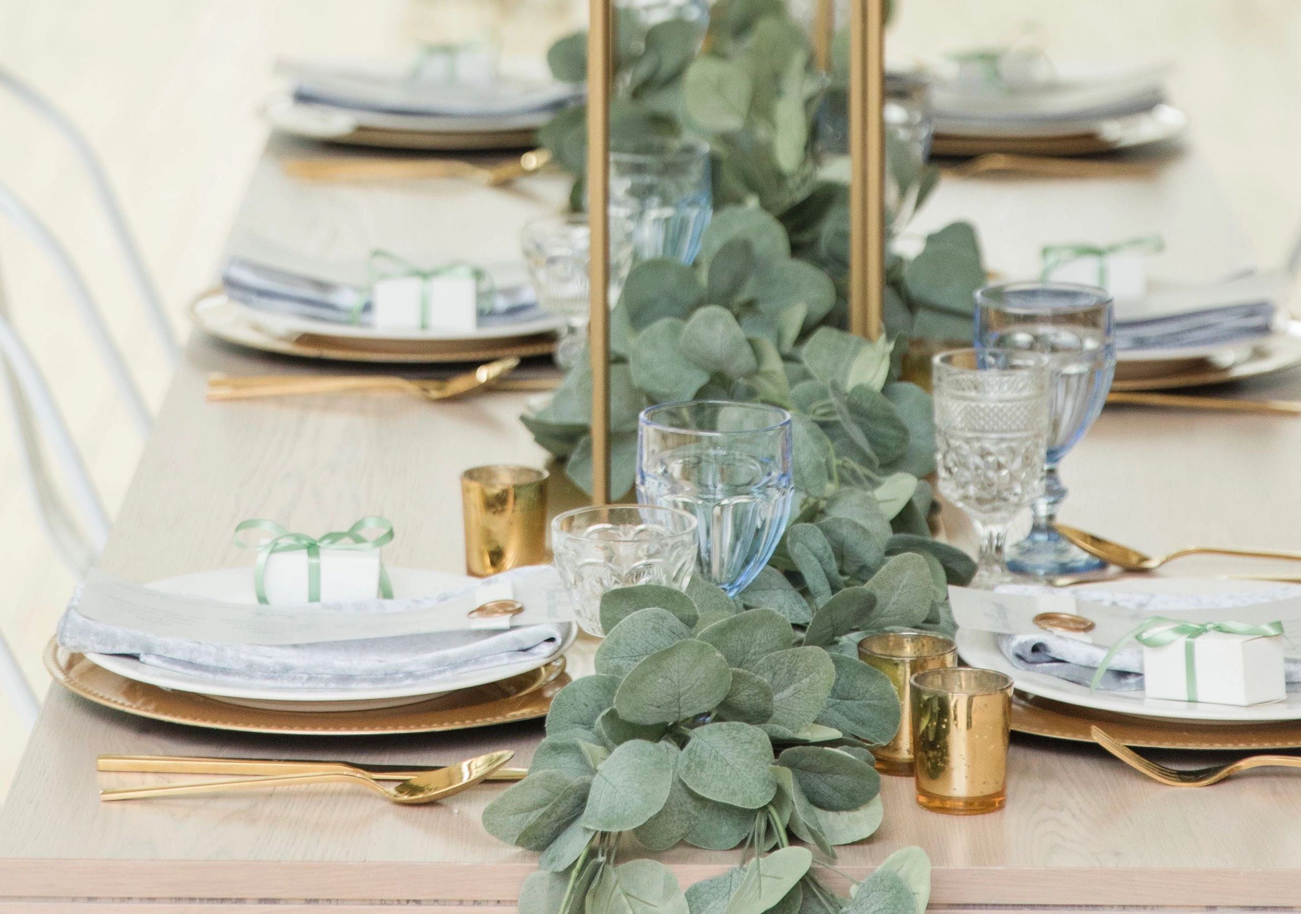 Elegantly set dining table with green foliage centerpiece and gold accents.