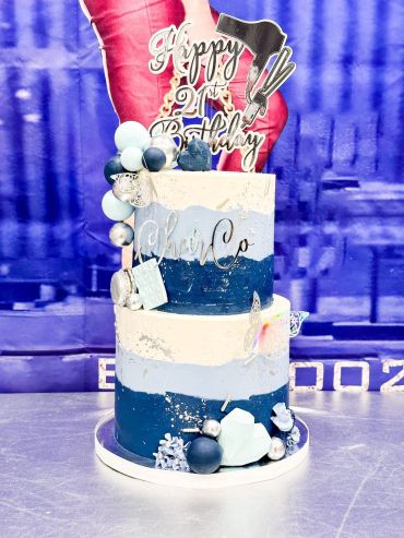 Two-tier blue and white birthday cake with decorative balls and topper.