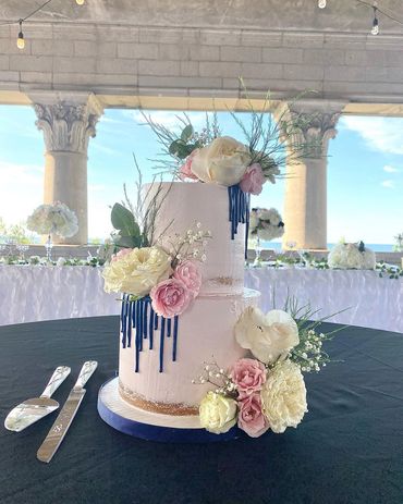 Elegant two-tier cake decorated with flowers and blue drizzle.