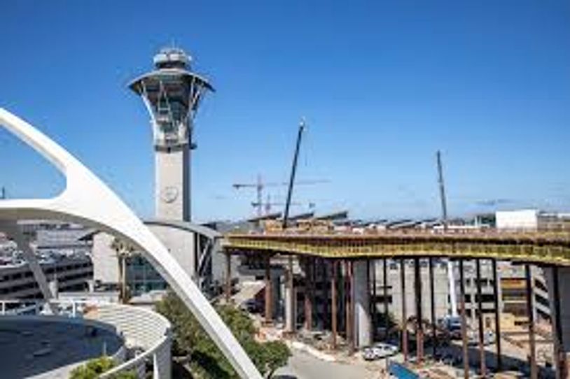 Airport control tower with ongoing construction nearby under clear blue sky.