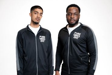 Two men wearing black jackets with "PURE VIBES ENT" logos standing against a white background.