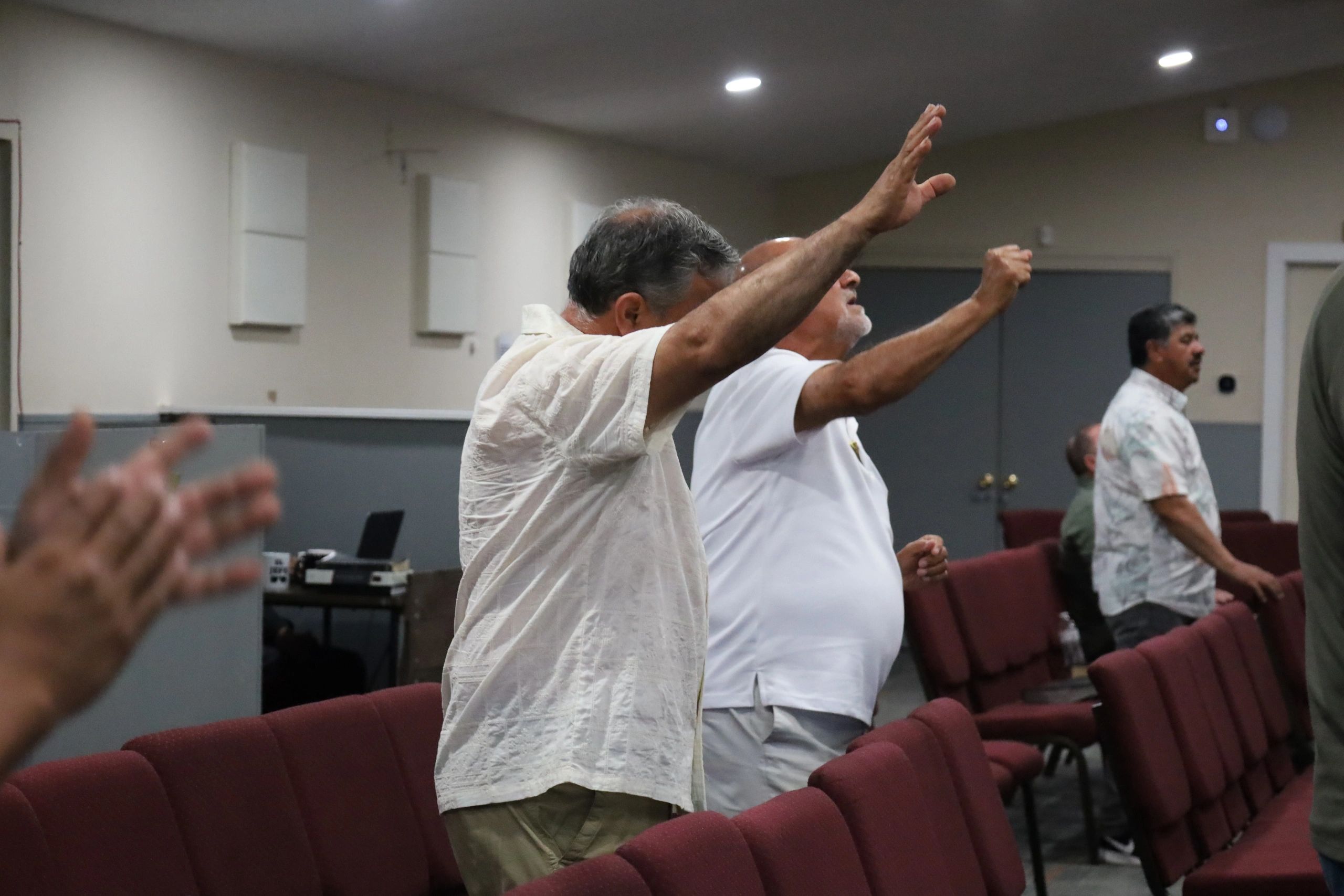 Men raising hands in a gathering or worship setting.
