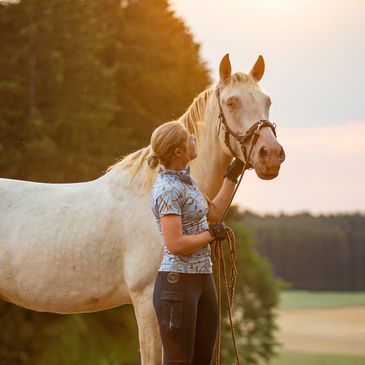Frau mit weißem Pferd bei Sonnenuntergang.