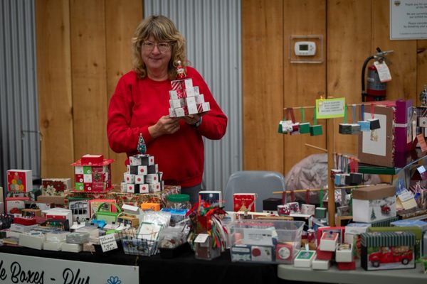 A woman in a red sweater stands behind a table displaying festive holiday boxes and decorations.