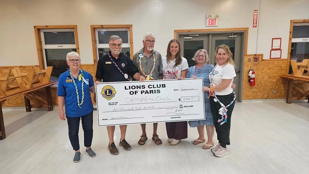 Group of six people holding a large Lions Club donation check indoors.