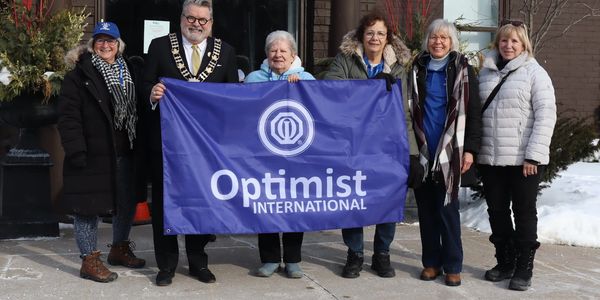 Group holding Optimist International banner outdoors in winter.