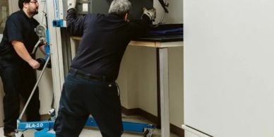 Two men moving a large machine using a lifting device in a workshop.