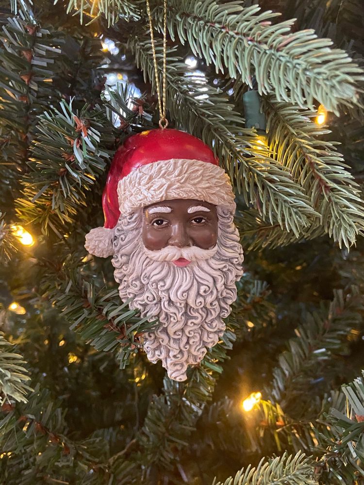 Close up of a green Christmas tree with a Black Santa ornament hanging from a branch.