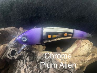 A purple and chrome fishing lure named Chrome Plum Alien on a natural wood background.