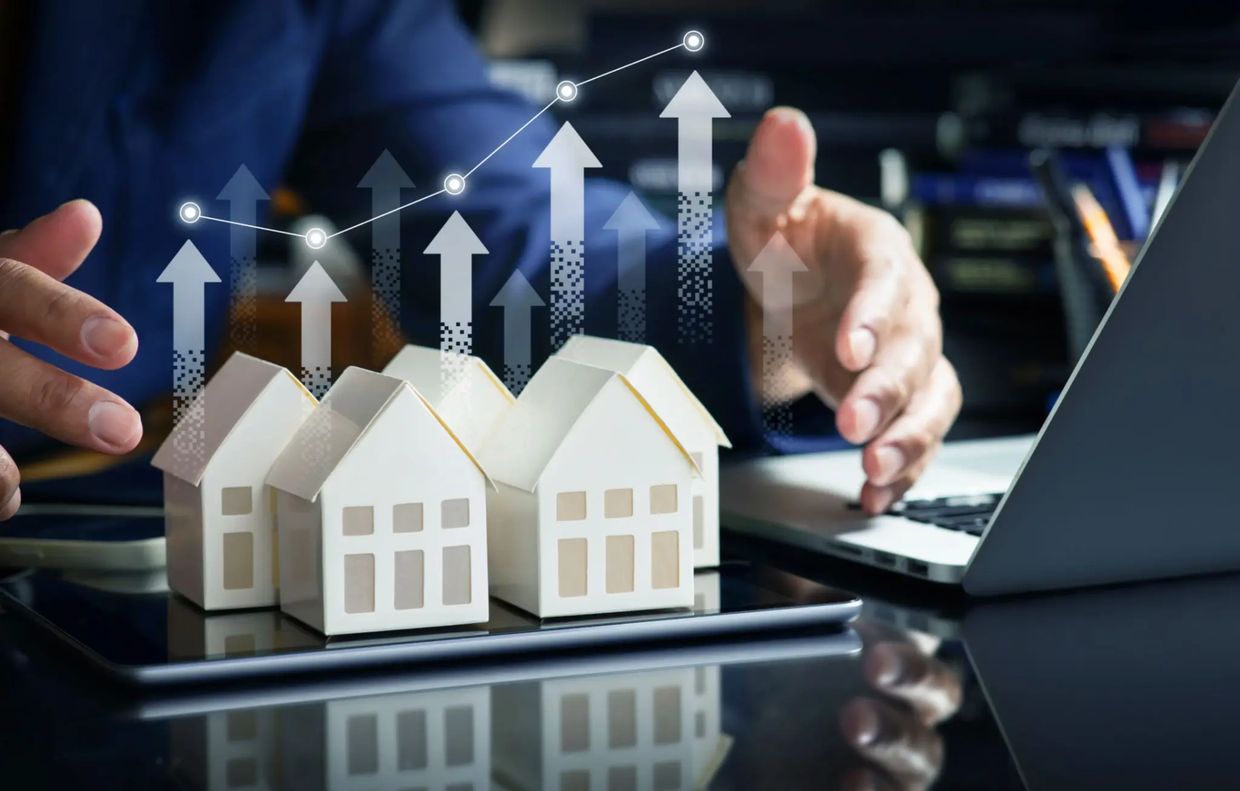 Small model houses with upward arrows and a laptop in the background.