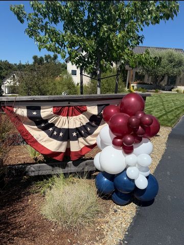 Patriotic red, white, and blue balloons with a star-spangled banner outdoors.
