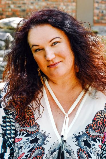 Smiling woman with curly hair in a patterned blouse.