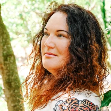 Woman with curly hair outdoors looking thoughtful.