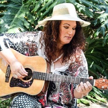 Woman playing acoustic guitar outdoors.