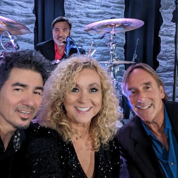 Four musicians posing on stage, smiling for a selfie.