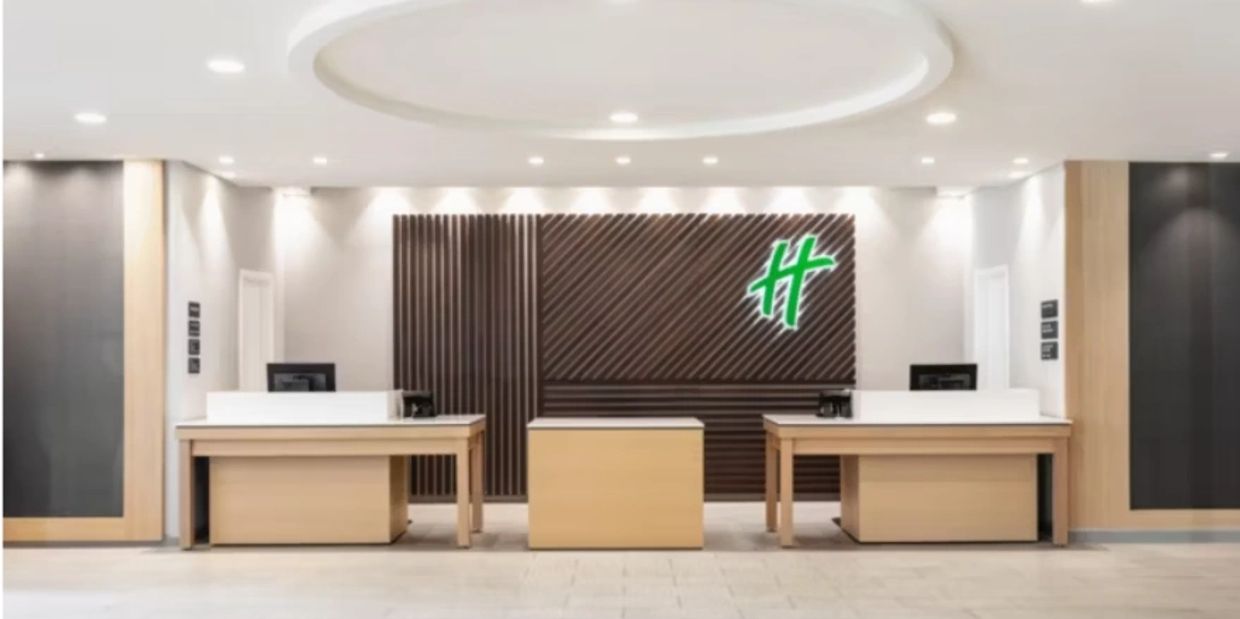Modern hotel reception with wooden desks and green illuminated logo.