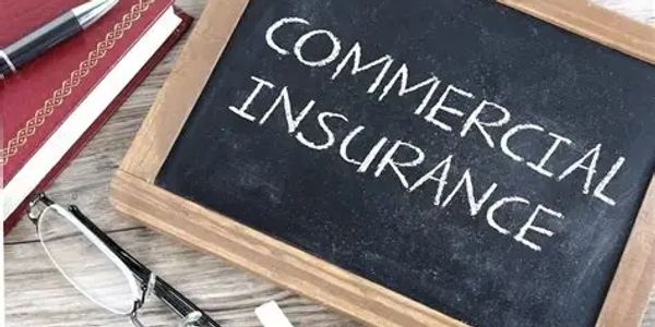 Chalkboard with 'Commercial Insurance' written, glasses, pen, and notebook on a wooden surface.