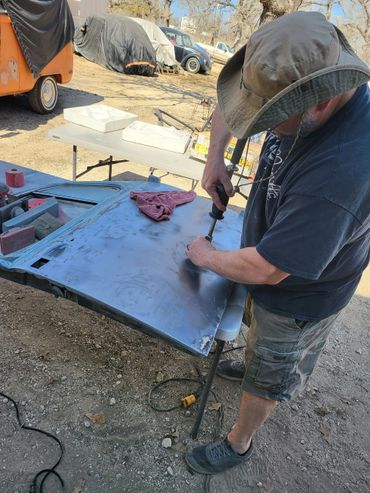 Man working on a metal car door outdoors with tools.