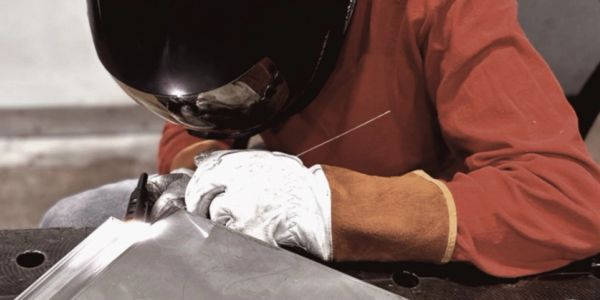 Person welding metal with protective gear in a workshop.