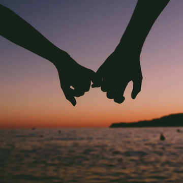 Dos manos de pareja agarradas y conectadas durante el atardecer.