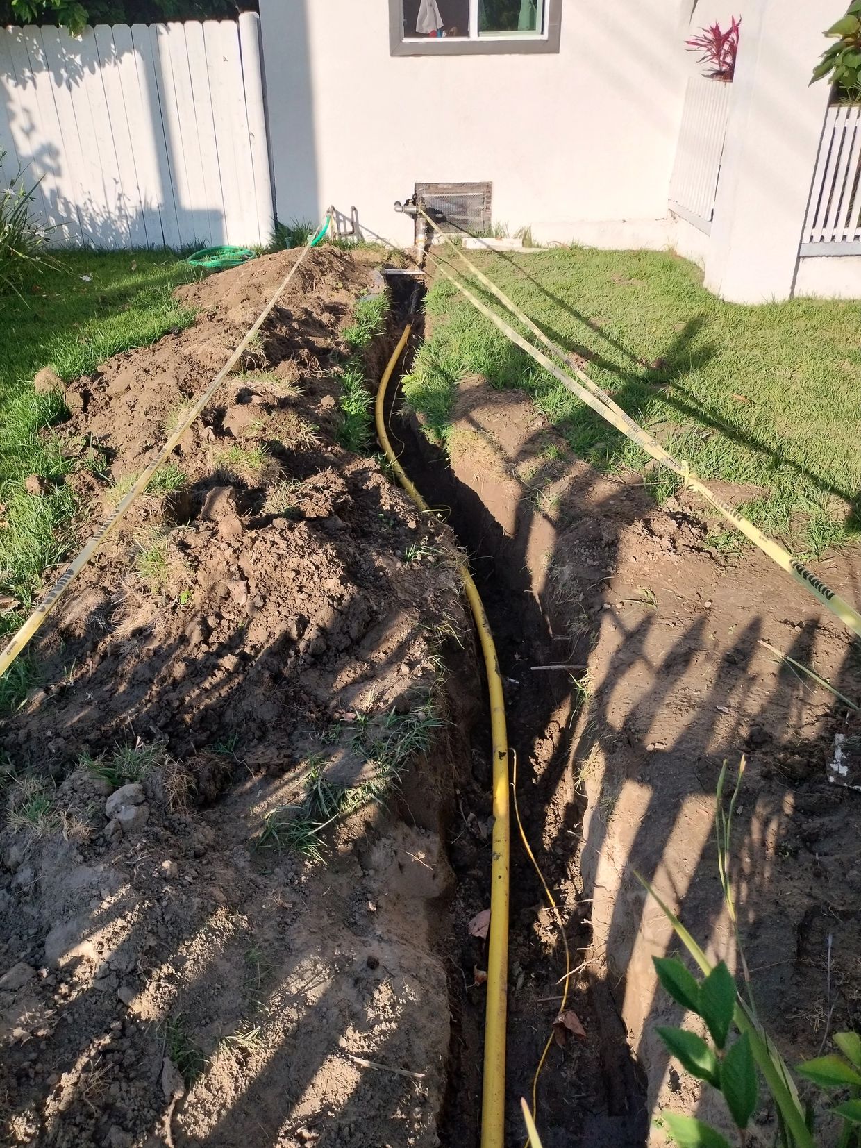 Trench with yellow pipe being laid in yard.