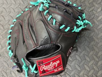 Black Rawlings baseball glove with teal laces on a textured surface.