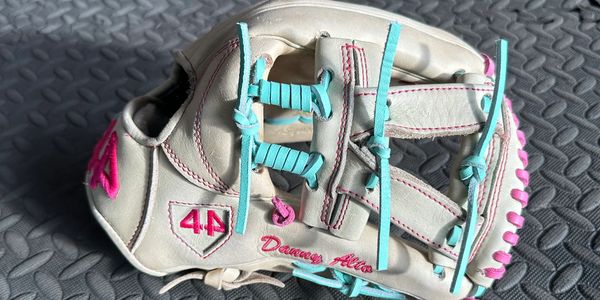 White baseball glove with blue laces and pink accents on a textured surface.