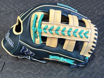 Close-up of a black and tan Wilson baseball glove with teal lacing.