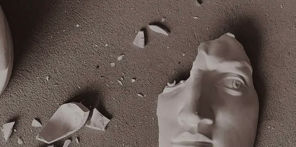 Une sculpture de visage cassée sur un sol poussiéreux.