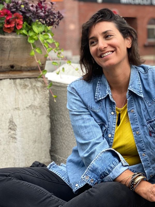 A smiling woman in a denim jacket sitting outdoors near flowers.