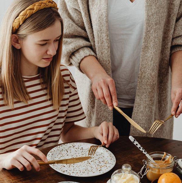 A girl and an adult preparing to eat at a table with utensils and food.