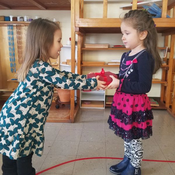 Two young girls exchanging a red gift box indoors.