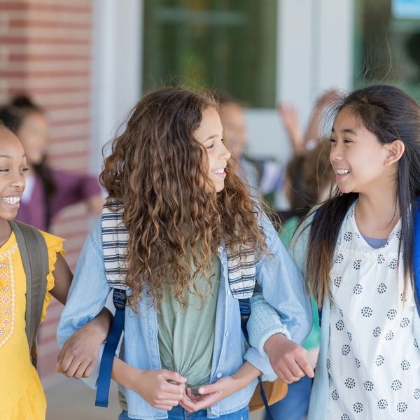 Three girls holding hands and smiling together at school.