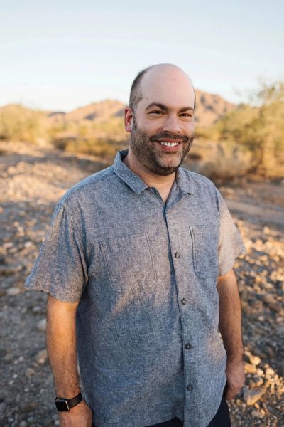 Smiling man standing outdoors in a rocky desert.