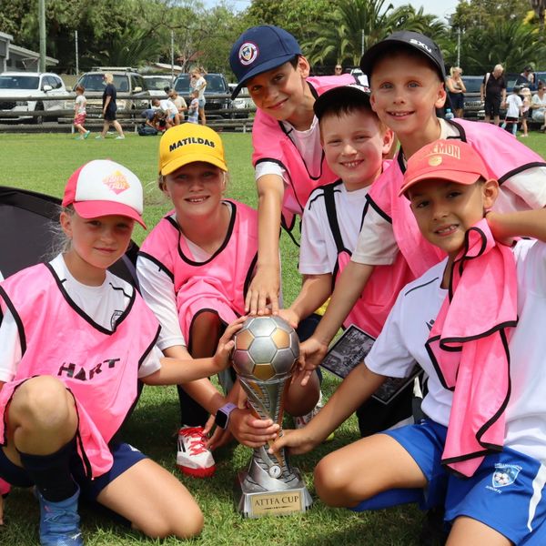 Young soccer players proudly hold a trophy on a sunny field.