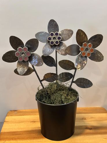 Metal flower sculpture with three flowers in a black pot on a wooden table.