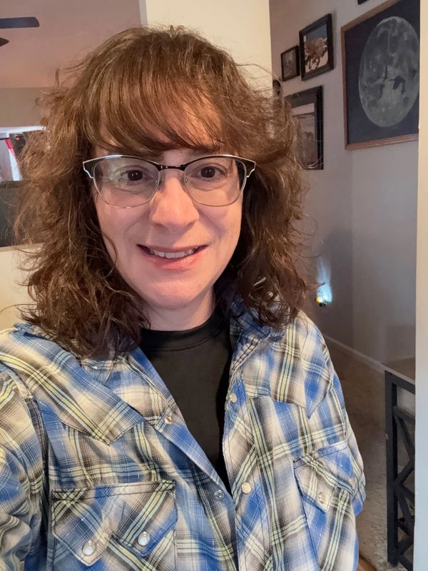 Smiling woman wearing glasses and a blue plaid shirt indoors.
