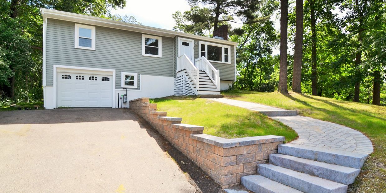 A gray house with a white garage door and a curved stone pathway.