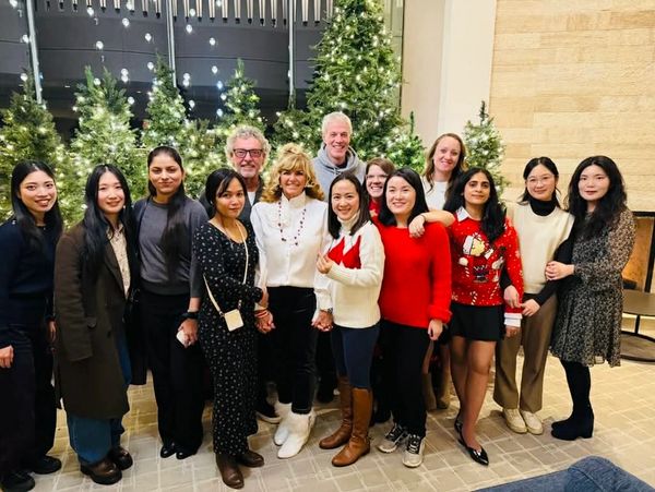 Group photo of diverse people in festive attire with decorated Christmas trees.