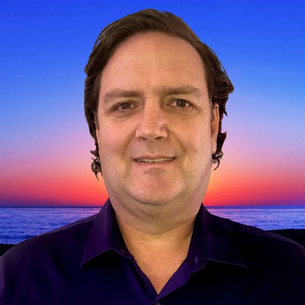 The owner, Erik Greiner, with a colorful image of the ocean at sunset, in the background.