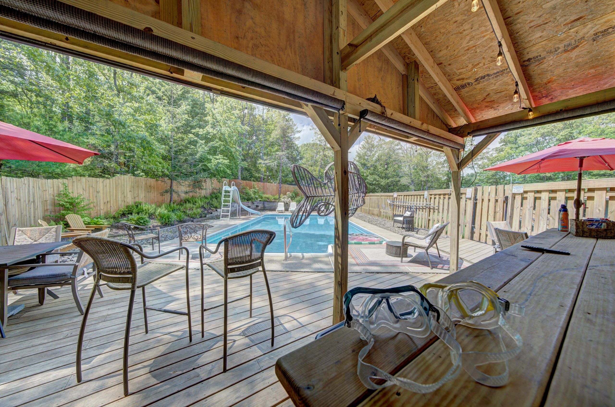 Pool area with chairs and umbrellas under a wooden gazebo.