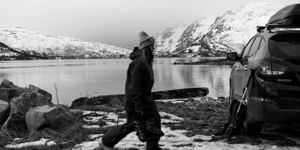 Person walking with skis near a car by a snowy lake.