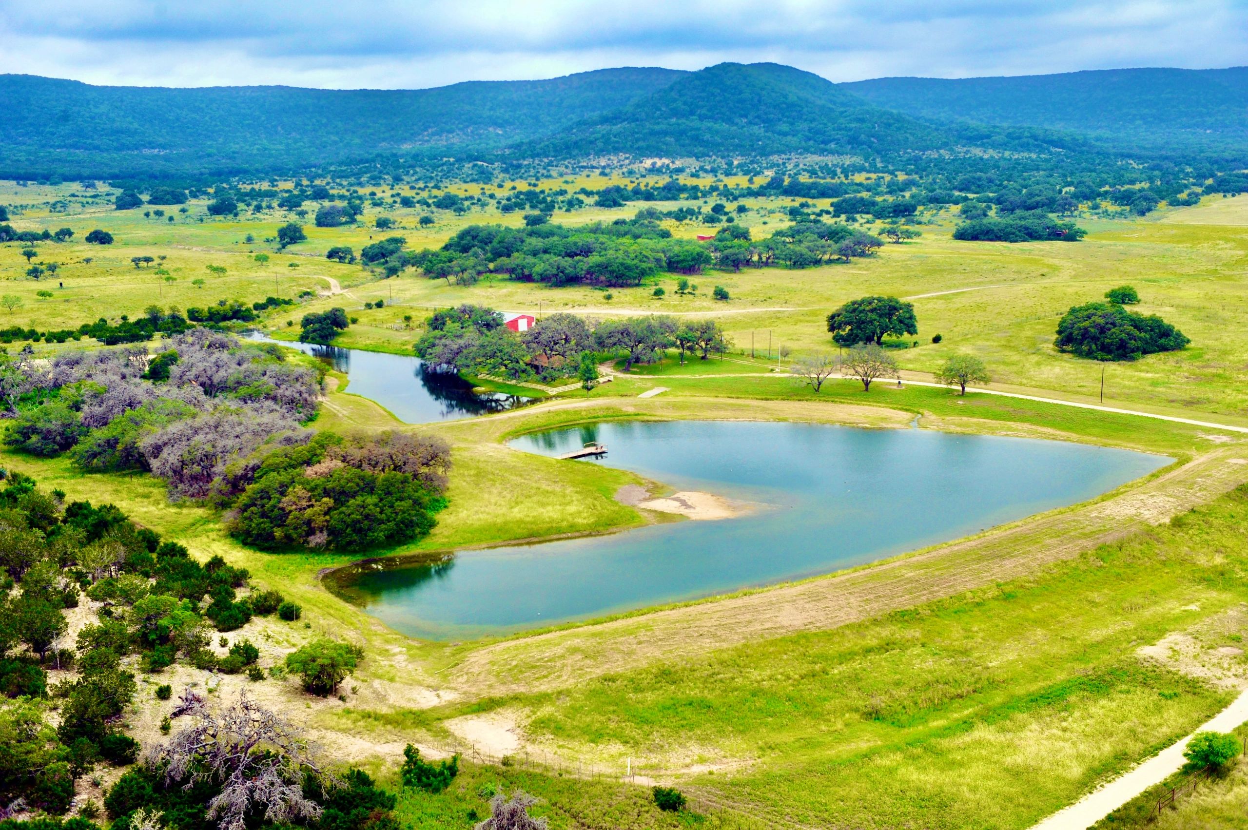 3R Sodbusters pond surrounded by green grass with a beautiful view of the Hill Country
